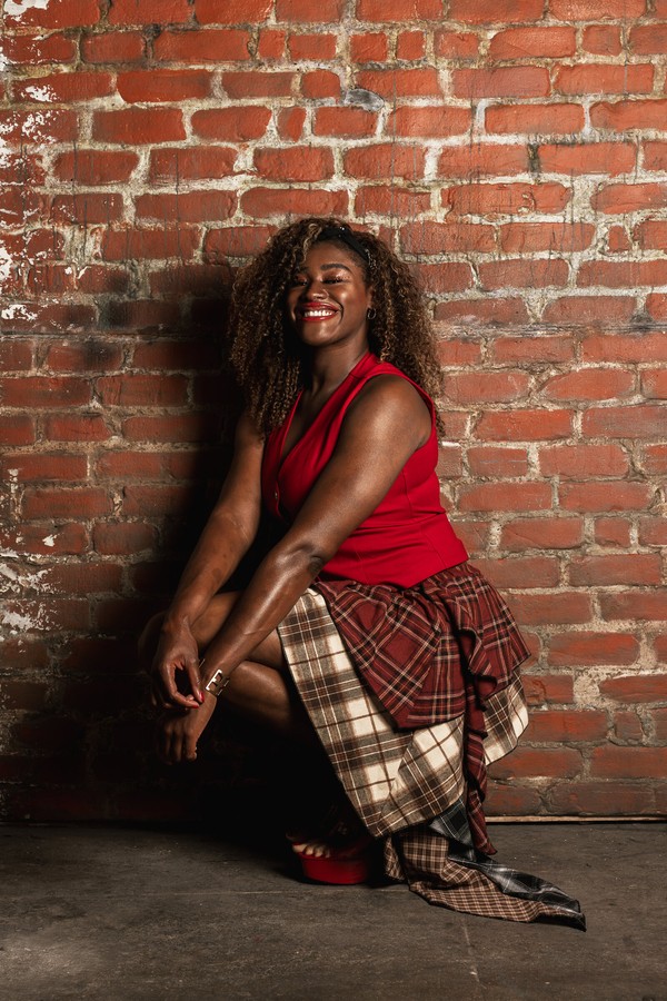 folasade Portrait of Folasade, director, writer and star of Keepers of the Door, crouching and smiling in front of a brick wall.