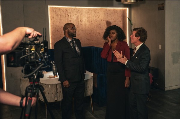 keepers-of-the-door-06 On set, an actress on the phone talks with two men in suits, facing the crew’s camera.